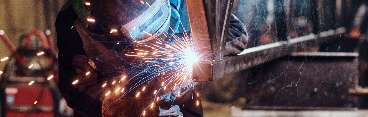 Man is working at metal factory, he is welding a piece of rail using special tools.